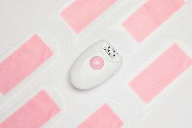 Modern epilator and wax strips on white background, flat lay