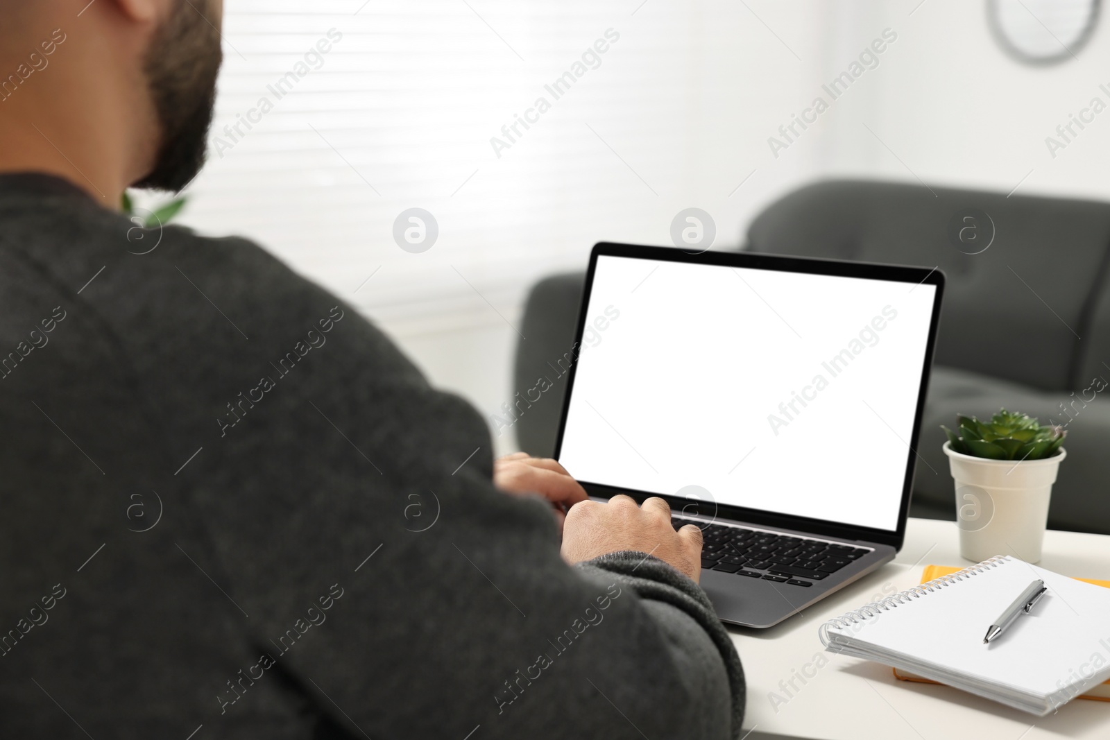 Photo of E-learning. Young man using laptop at white table indoors, closeup