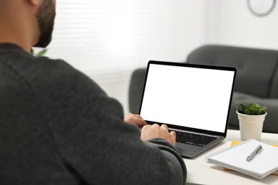 Photo of E-learning. Young man using laptop at white table indoors, closeup