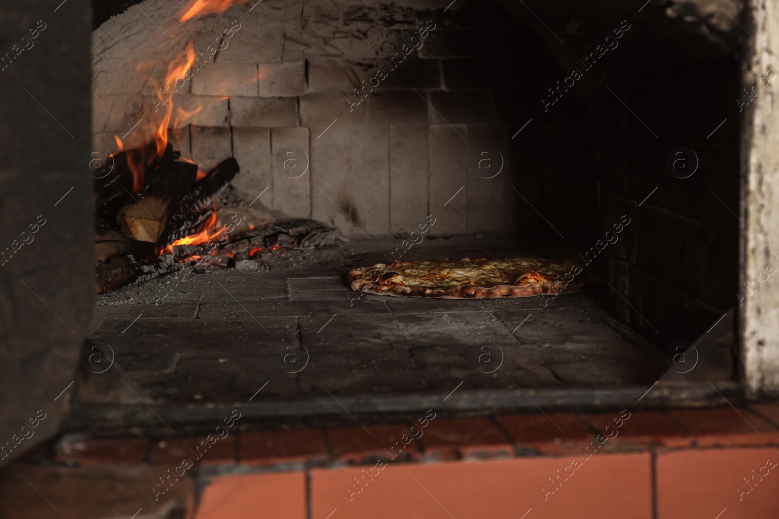 Photo of Burning firewood and tasty pizza in oven at restaurant kitchen