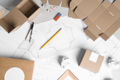 Photo of Creating packaging design. Drawings, boxes and stationery on light wooden table, flat lay