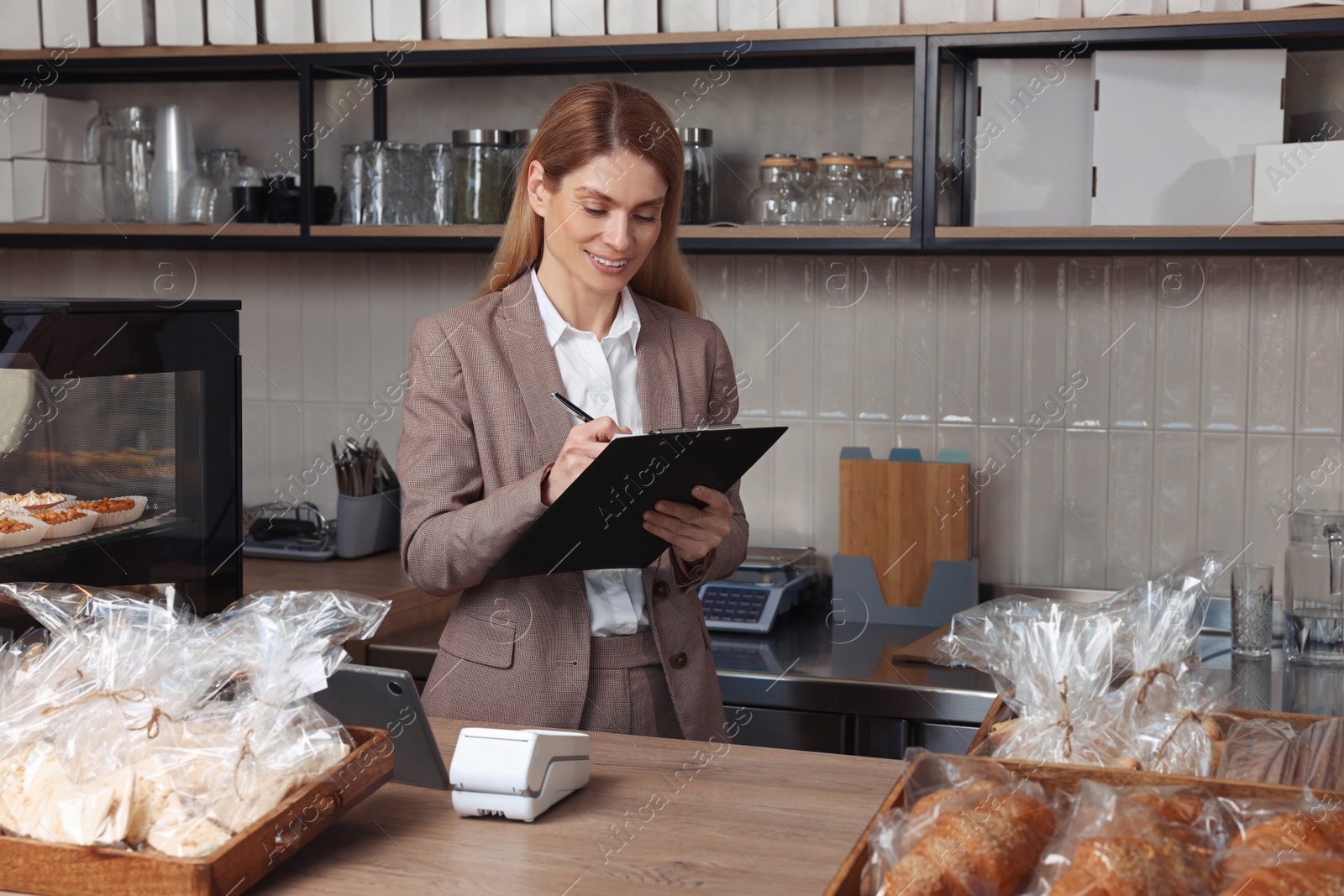 Photo of Happy business owner with clipboard and pen at cashier desk in bakery shop