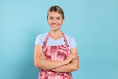 Photo of Beautiful young woman in clean striped apron on light blue background