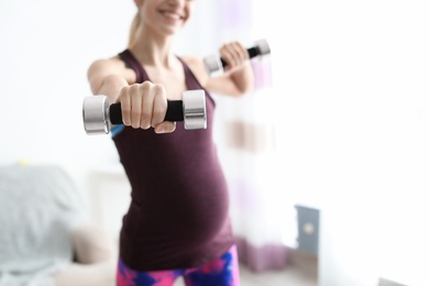 Photo of Young pregnant woman doing exercises with dumbbells at home