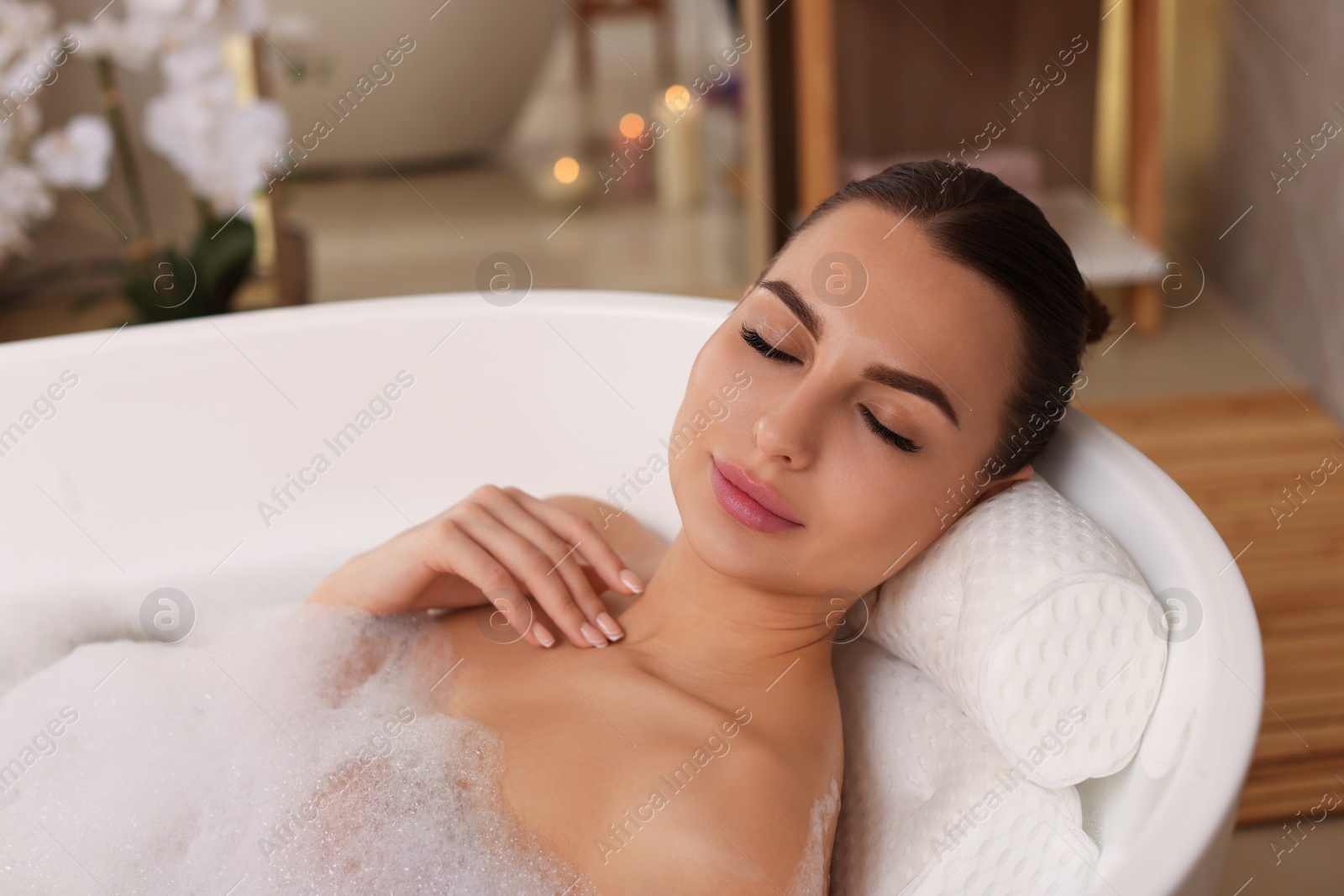 Photo of Young woman using pillow while enjoying bubble bath indoors