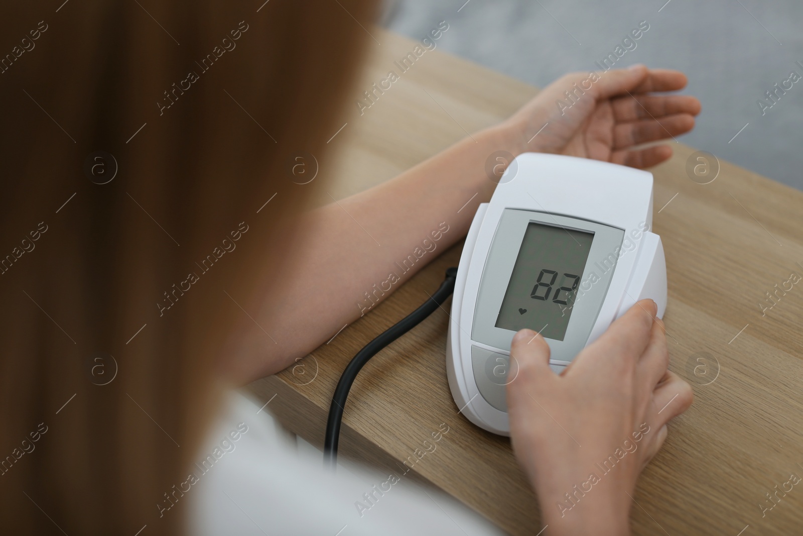 Photo of Woman checking blood pressure with sphygmomanometer at table indoors, closeup. Cardiology concept