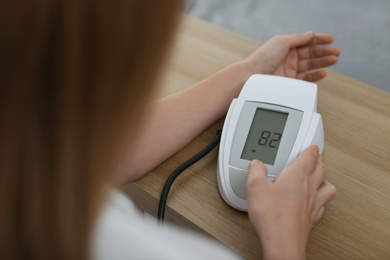 Woman checking blood pressure with sphygmomanometer at table indoors, closeup. Cardiology concept