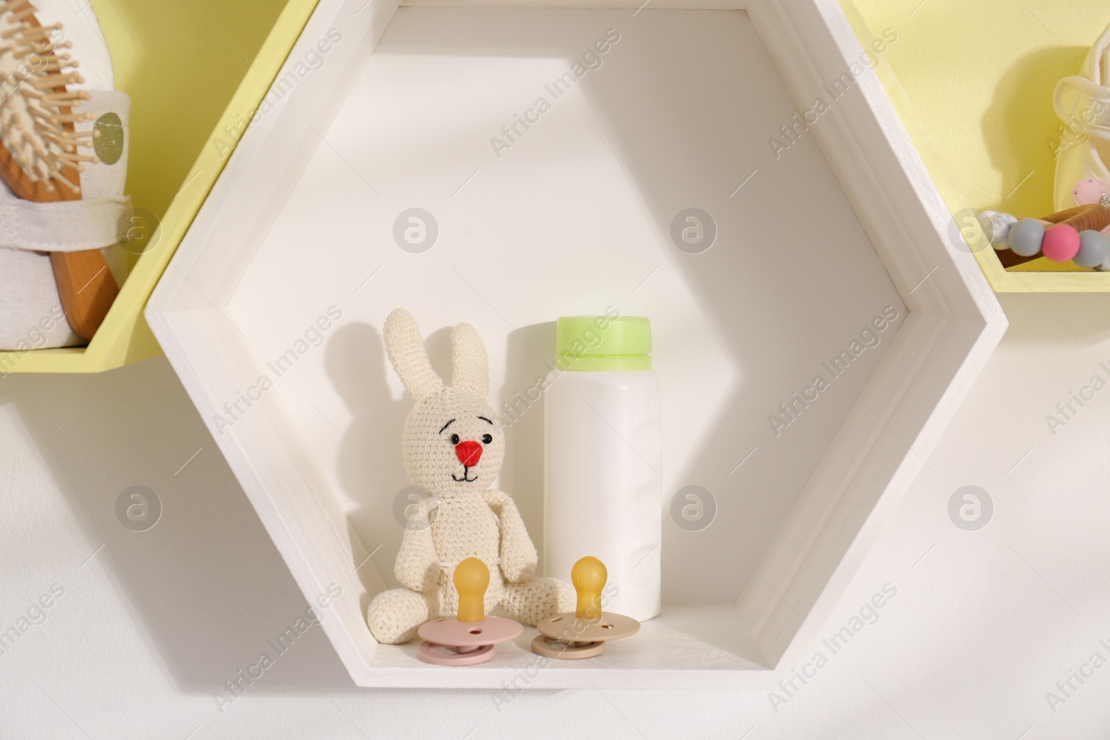 Photo of Hexagon shaped shelves with toys and child's accessories on white wall. Interior design