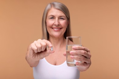 Photo of Beautiful woman with vitamin capsule and glass of water on beige background, selective focus