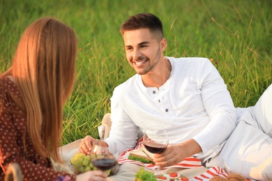 Happy young couple with wine having picnic in green park