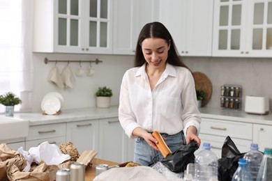 Photo of Garbage sorting. Woman putting food waste into plastic bag at table in kitchen