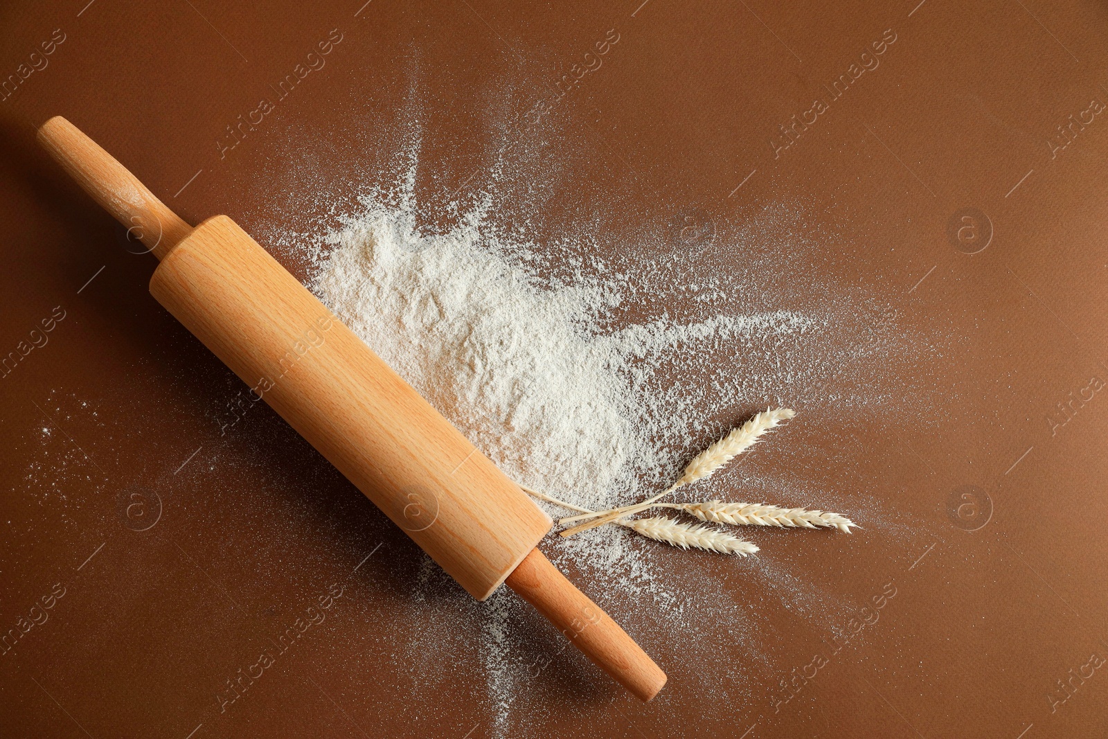 Photo of Flour, spikelets and rolling pin on brown table, top view. Space for text