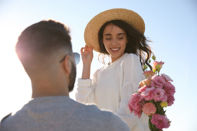 Photo of Young man giving flowers to his wife against blue sky. Honeymoon trip