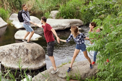 Photo of Group of young people crossing river. Camping season