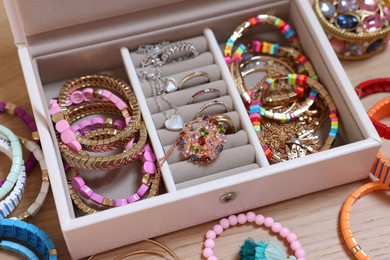 Photo of Jewelry box with stylish bracelets and other accessories on wooden table, closeup