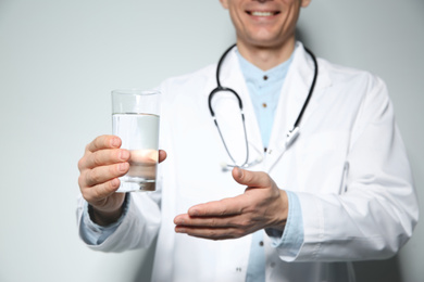 Photo of Nutritionist holding glass of pure water on light grey background, focus on hand