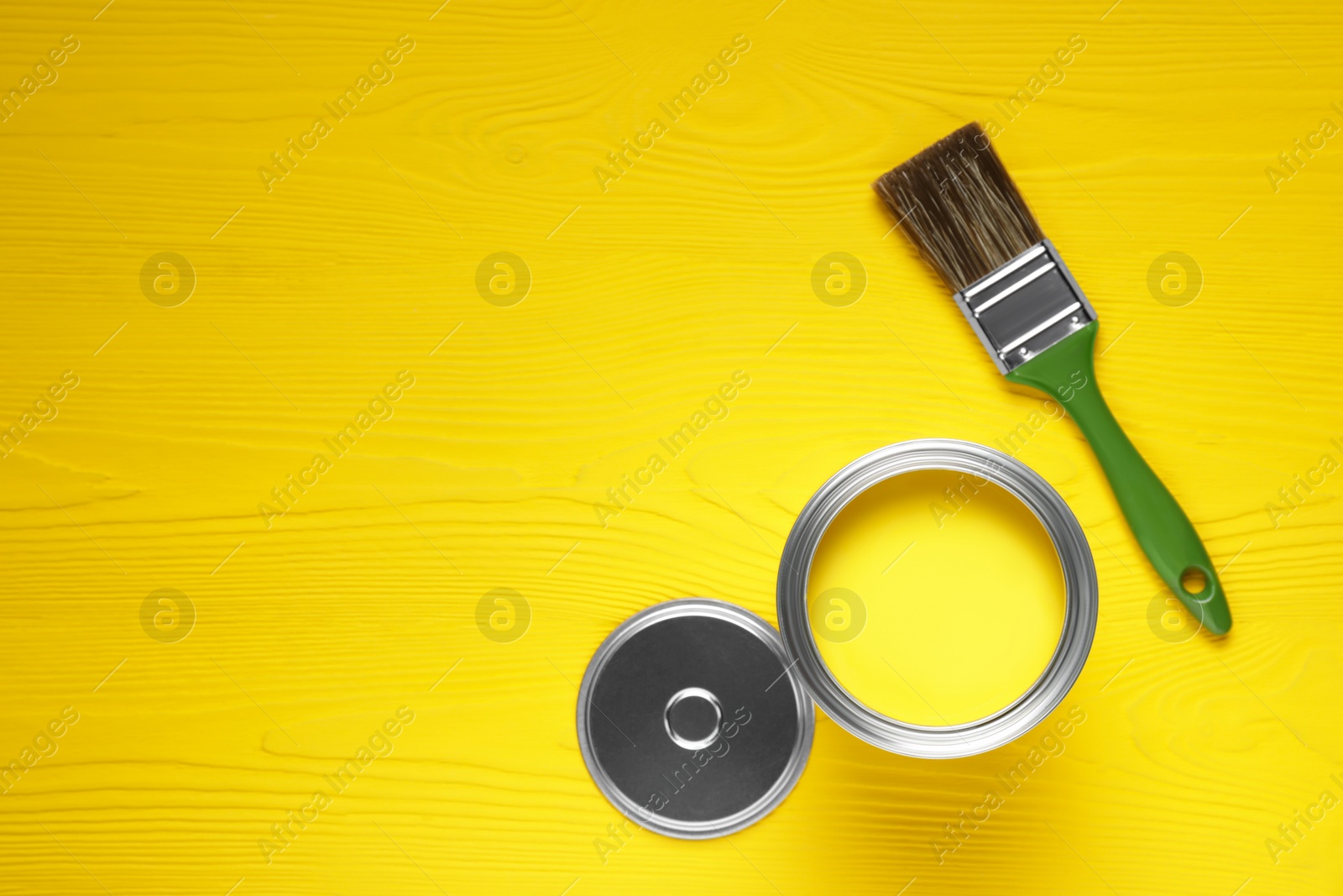 Photo of Can of yellow paint and brush on wooden table, flat lay. Space for text