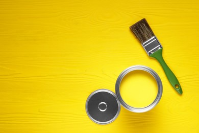 Can of yellow paint and brush on wooden table, flat lay. Space for text