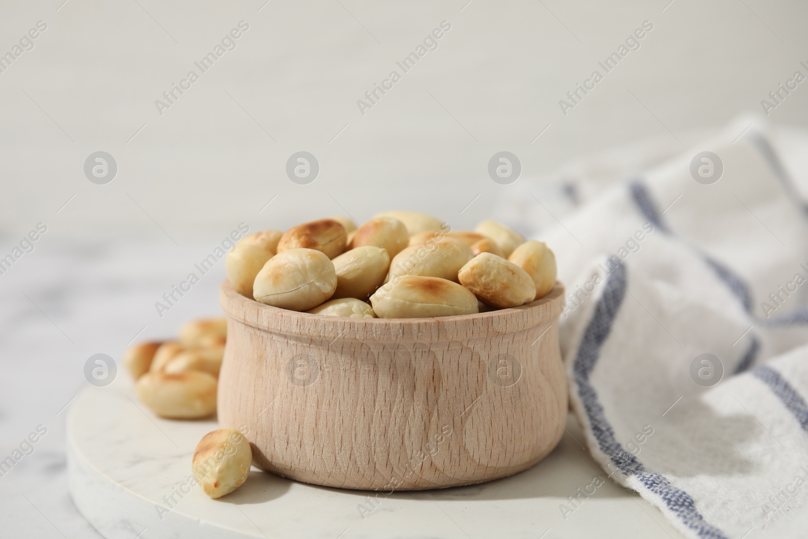 Photo of Roasted peanuts in bowl on white table, closeup