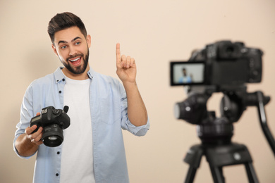 Photo of Young blogger with camera recording video against beige background