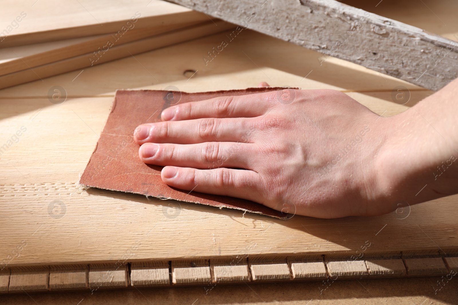 Photo of Man polishing wooden planks with sandpaper, closeup