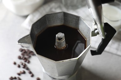 Photo of Brewed coffee in moka pot and beans on light grey table, closeup