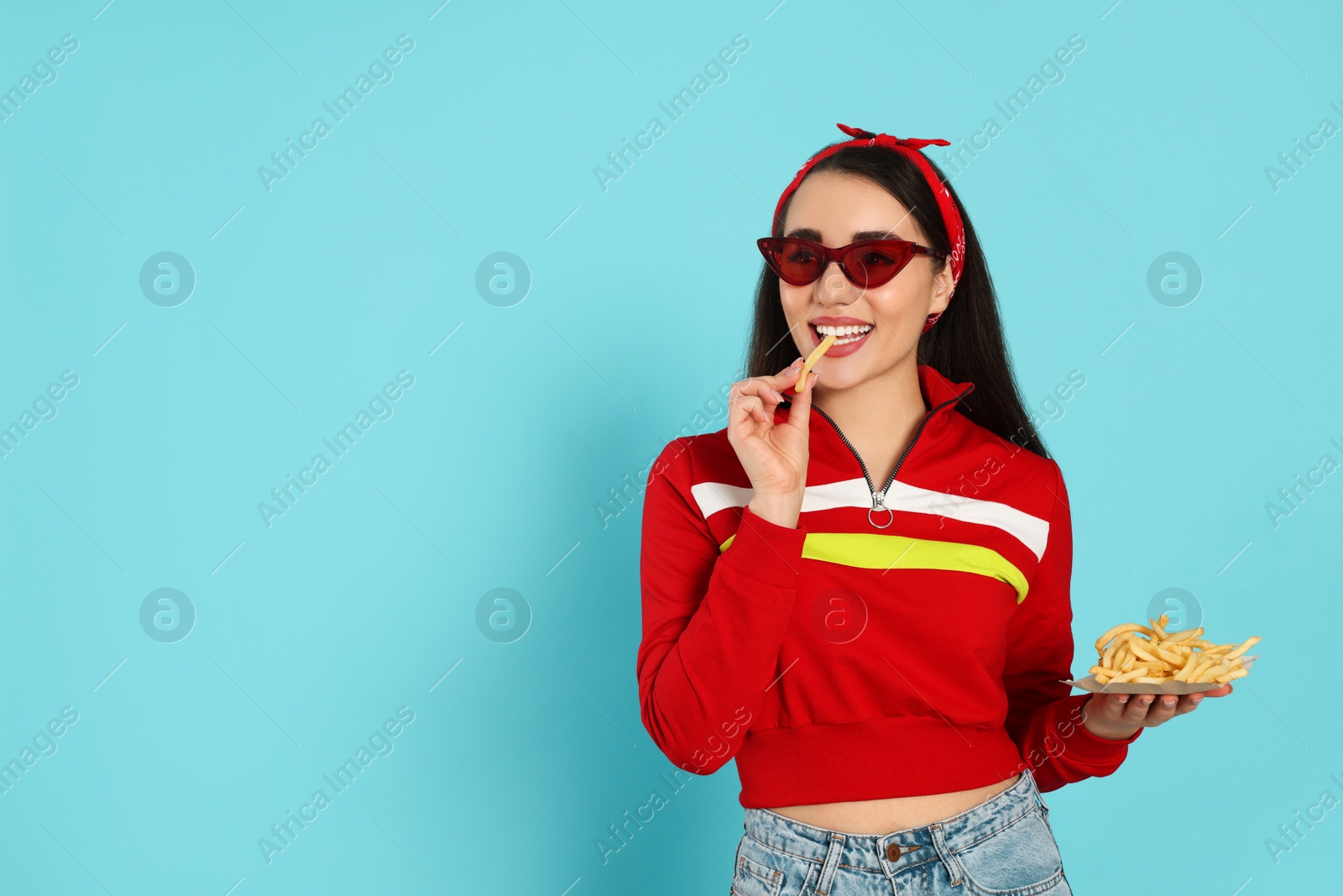 Photo of Beautiful young woman eating French fries on light blue background. Space for text