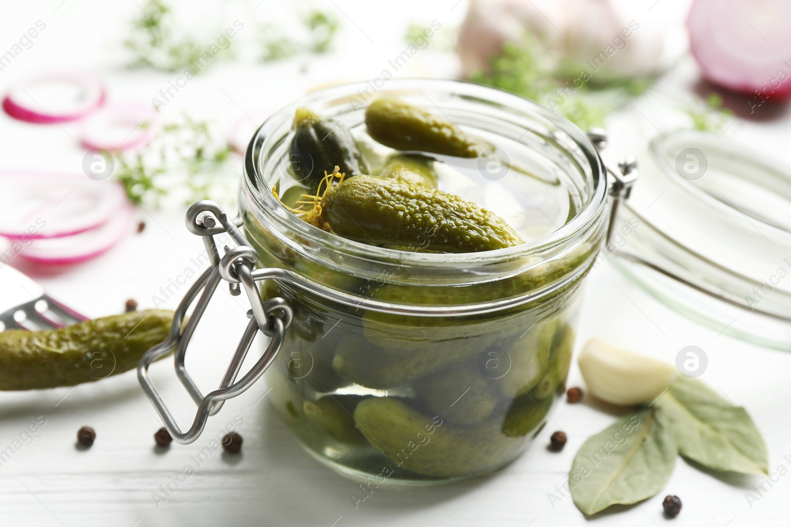 Photo of Glass jar of pickled cucumbers on white wooden table, closeup