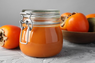 Photo of Delicious persimmon jam and fresh fruits on grey table, closeup