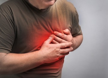 Senior man having heart attack on light grey background, closeup