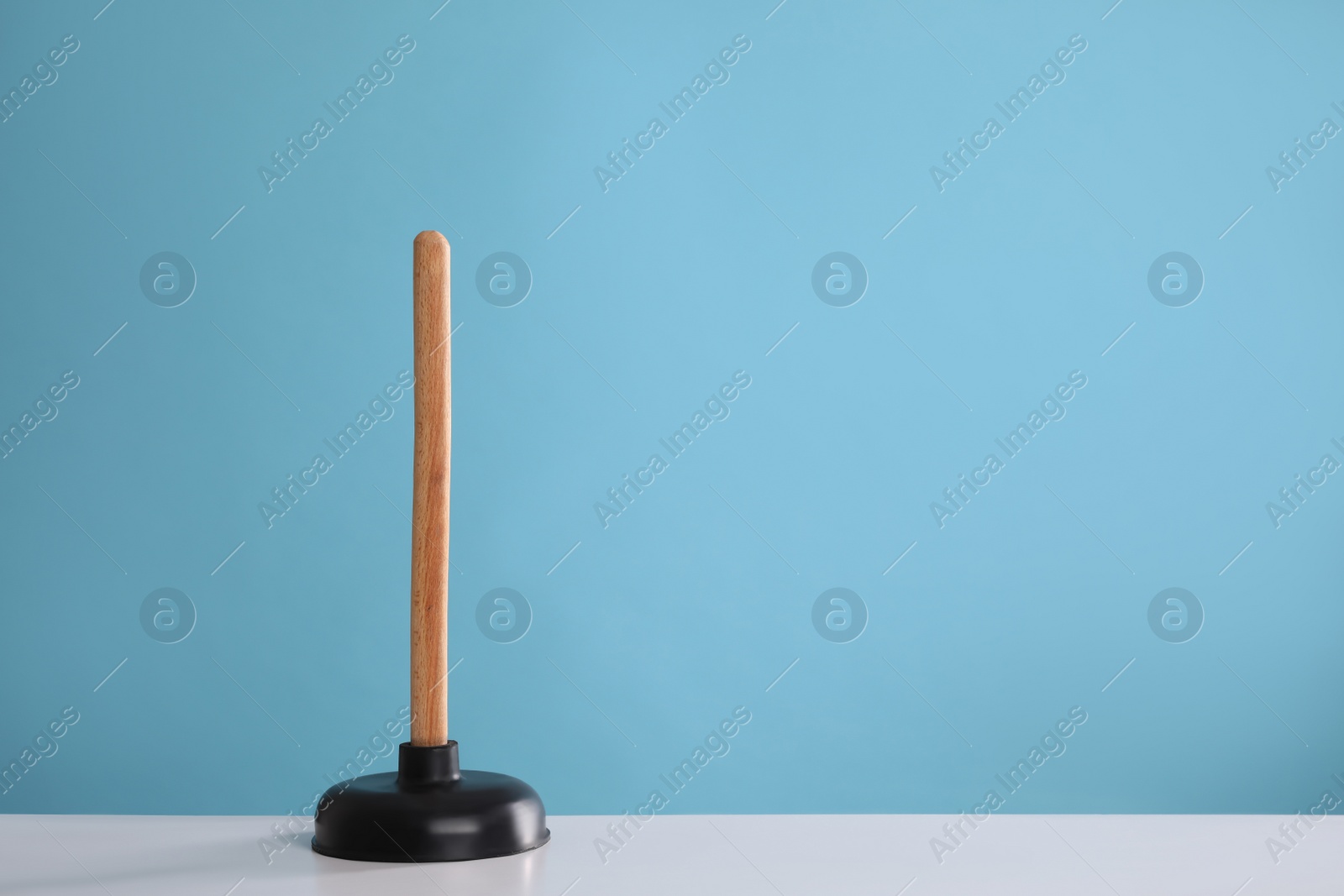 Photo of Plunger on white table against turquoise background. Space for text