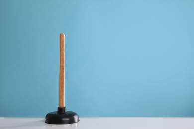 Photo of Plunger on white table against turquoise background. Space for text