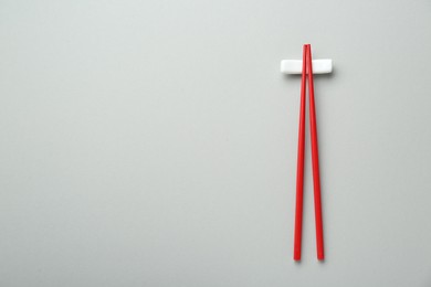 Photo of Pair of red chopsticks with rest on light grey background, top view. Space for text