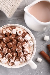 Photo of Cup of aromatic hot chocolate with marshmallows, and cocoa powder served on gray table, flat lay