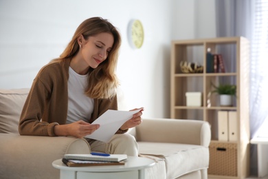 Happy woman reading letter on sofa at home