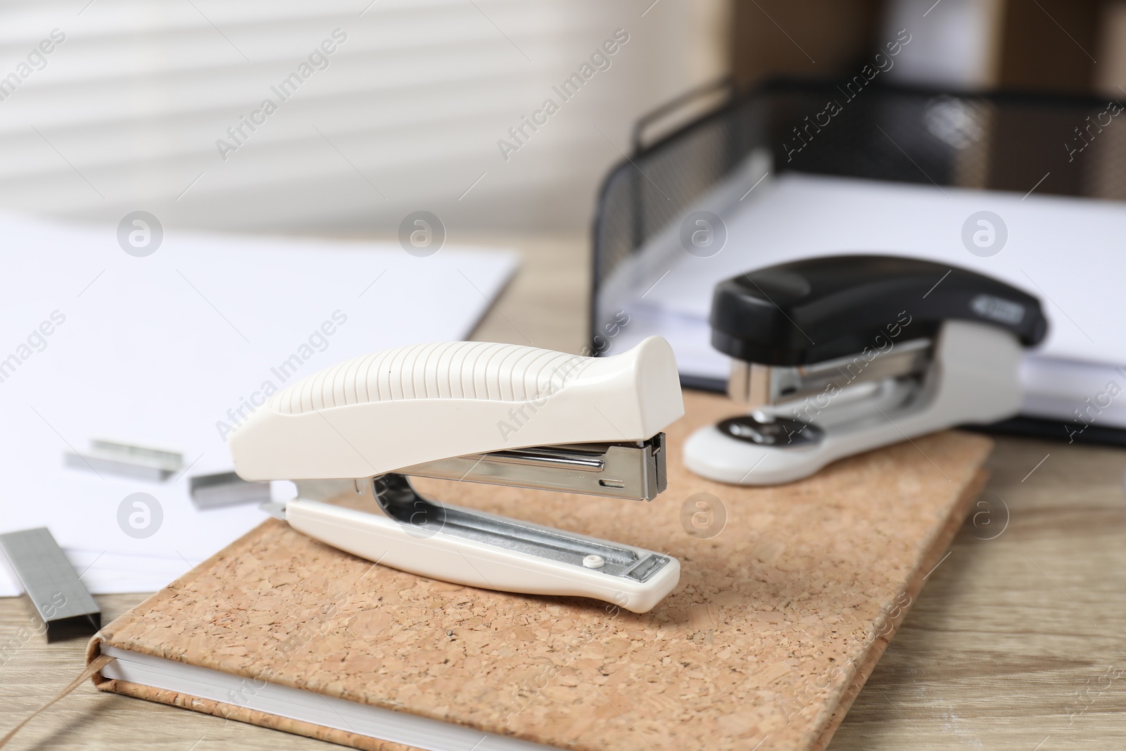 Photo of Staplers and notebook on wooden table indoors, closeup