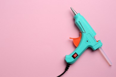 Turquoise glue gun with stick on pink background, top view. Space for text