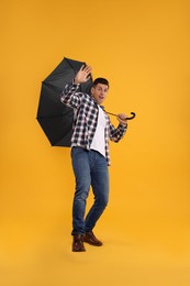 Emotional man with umbrella caught in gust of wind on yellow background
