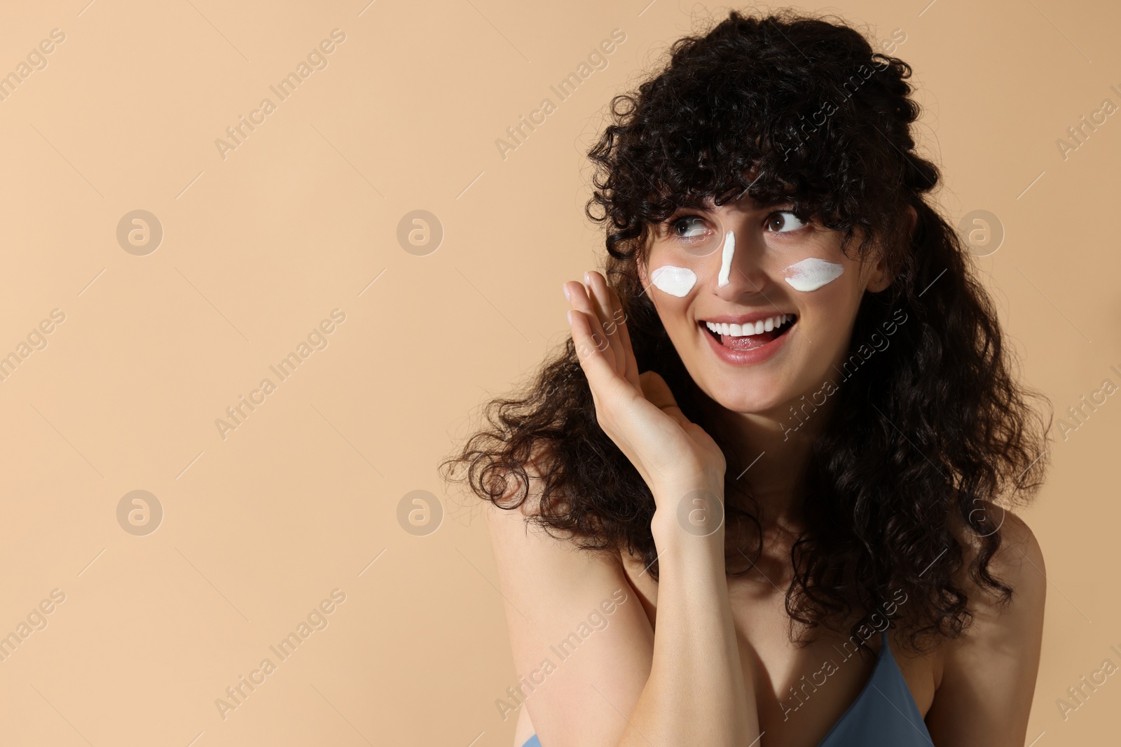 Photo of Beautiful young woman with sun protection cream on her face against beige background, space for text