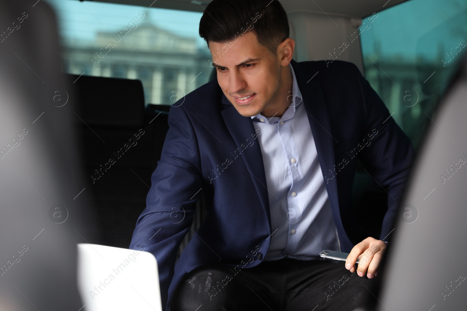 Photo of Handsome man working with laptop on backseat of modern car