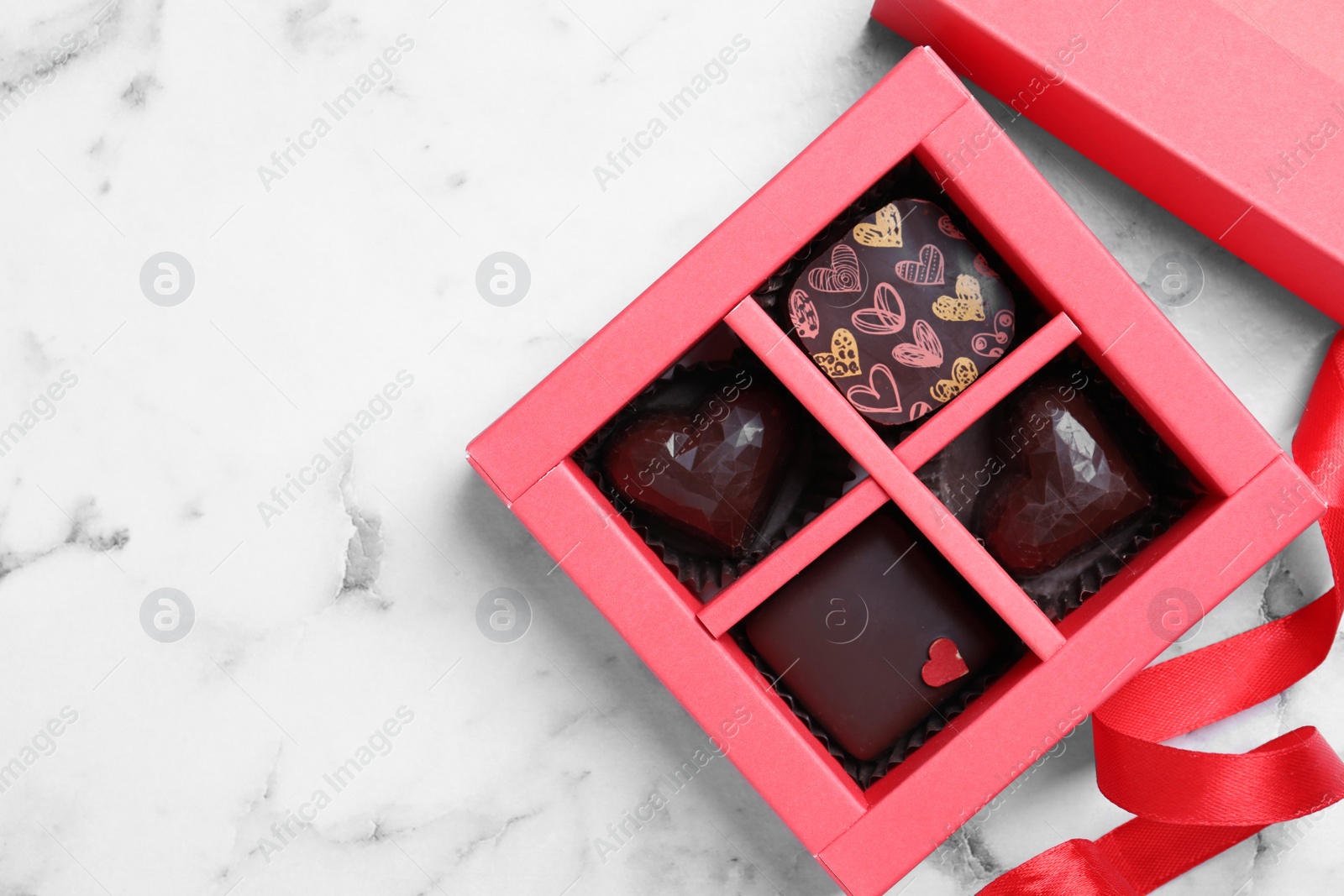 Photo of Box with tasty chocolate candies on white marble table, flat lay