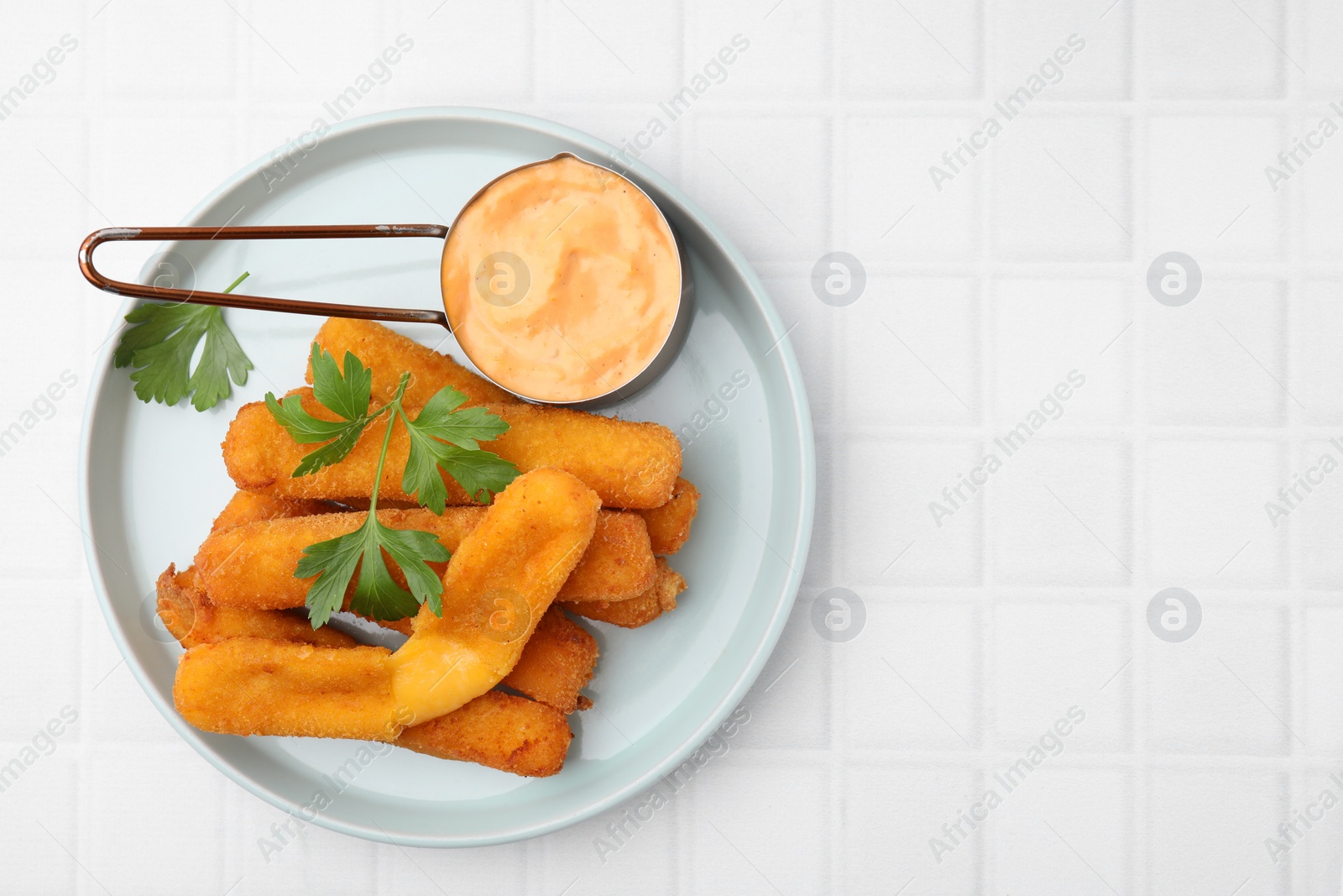 Photo of Tasty fried mozzarella sticks served with sauce and parsley on white tiled table, top view. Space for text