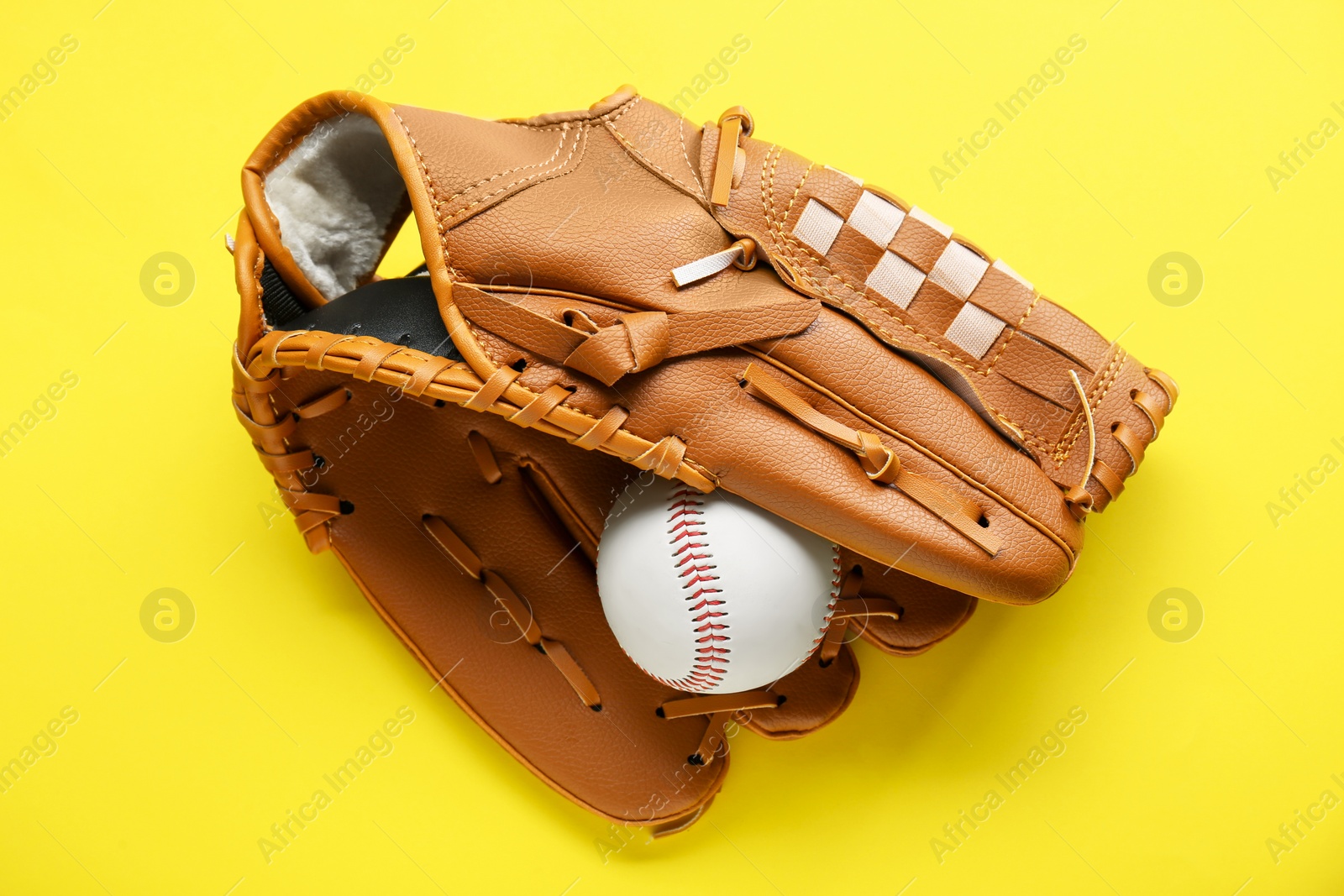 Photo of Catcher's mitt and baseball ball on yellow background, top view. Sports game