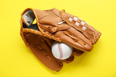 Catcher's mitt and baseball ball on yellow background, top view. Sports game