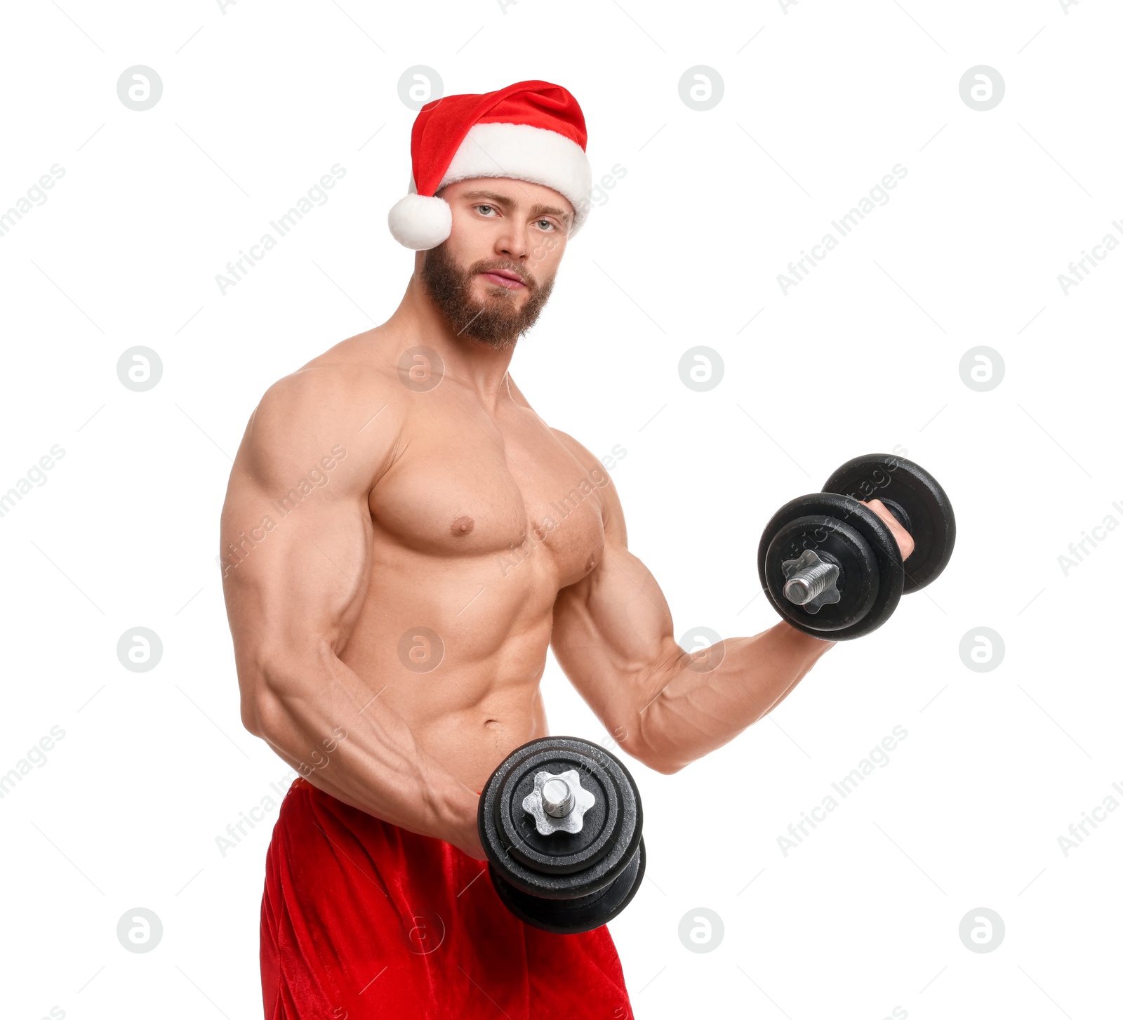 Photo of Attractive young man with muscular body in Santa hat holding dumbbells on white background