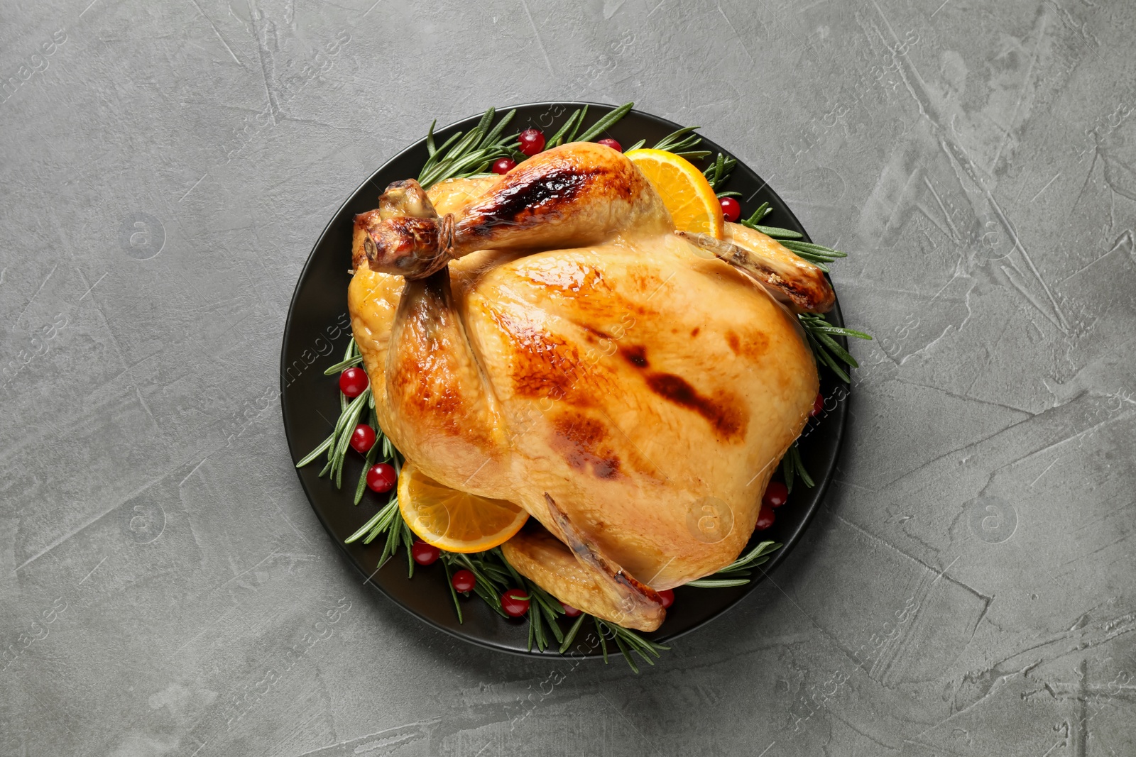 Photo of Delicious cooked turkey served with rosemary, oranges and cranberries on grey table, top view. Thanksgiving Day celebration
