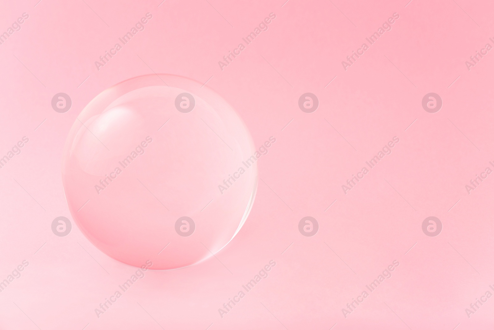 Photo of Transparent glass ball on light pink background. Space for text