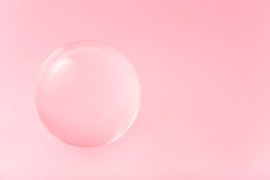 Transparent glass ball on light pink background. Space for text