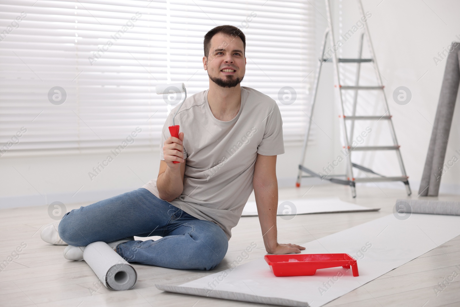 Photo of Man with roller, wallpaper and container in room
