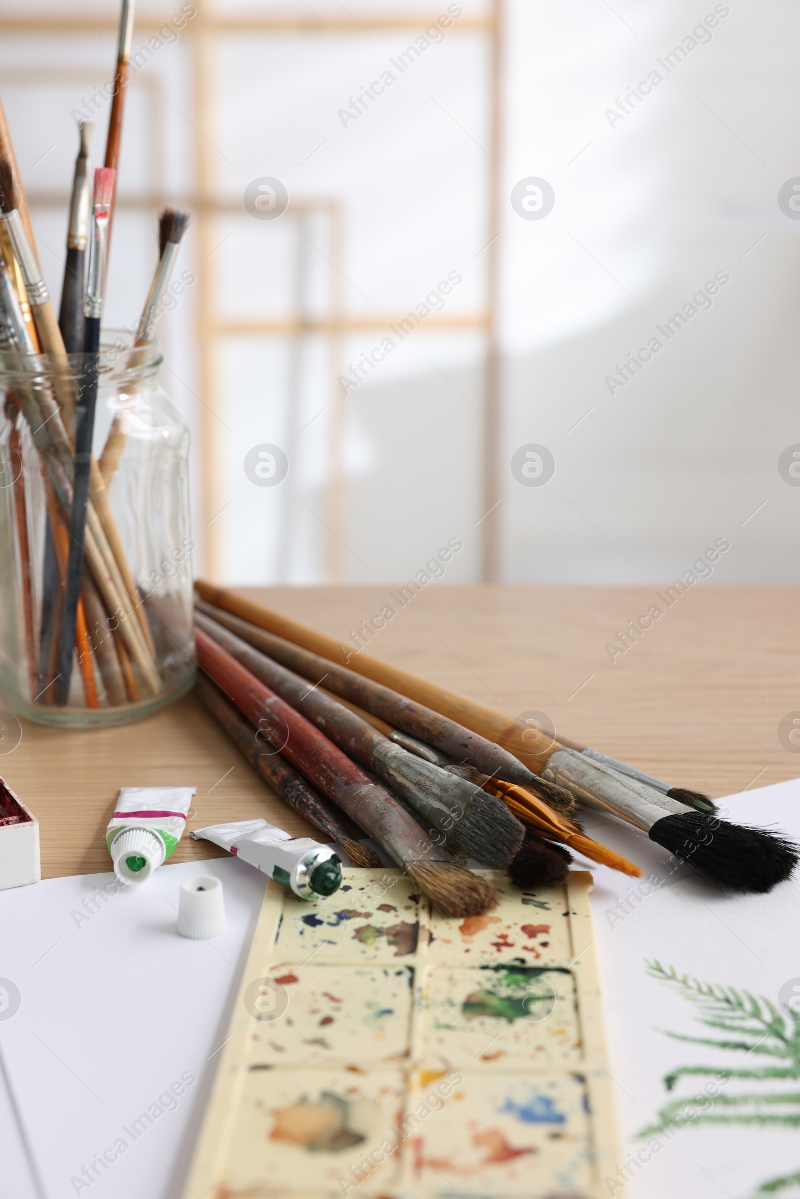 Photo of Different brushes, colorful paints, palette and drawing on table in studio. Artist's workplace